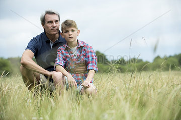 Father and son crouching together in tall grass