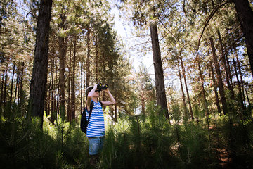 Boy looking through binoculars while hiking in woods