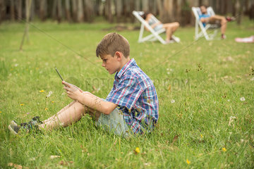 Boy sitting on lawn looking at digital tablet