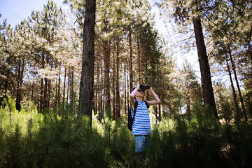 Boy looking through binoculars in woods