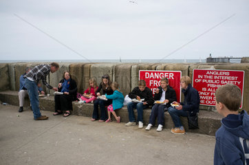 Whitby  Grossbritannien  Urlauber sitzen am Pier und essen Fish and Chips