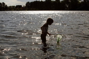 Wusterhausen  Deutschland  Junge steht mit einem Kescher im Wasser in einem See