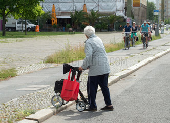 Eine Rentnerin beim Ueberqueren einer Strasse und eines Fahrradweges