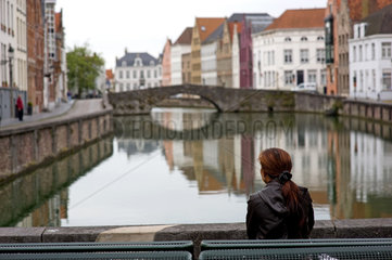 Bruegge  Belgien  eine Frau betrachtet eine Gracht  in der sich die Haeuser spiegeln
