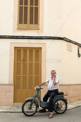 Campos  Mallorca  Spanien  aelterer Mann auf einem Moped telefoniert