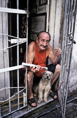 Havanna  Kuba  Mann sitzt mit Zeitung und seinem Hund rauchend in der Tuer