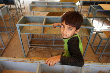 Kunduz  Afghanistan  Junge sitzt inmitten von Schulbaenken