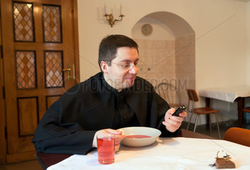 Krakau  Polen  Priester prueft die SMS seines Handys beim Essen