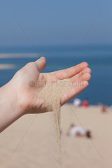 Arcachon  Frankreich  Tourist laesst den Sand der Dune du Pilat durch die Hand rieseln