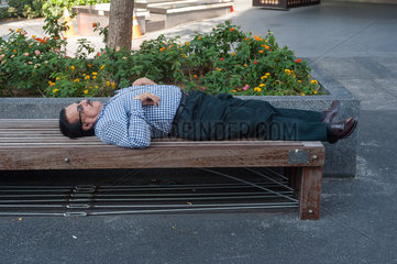 Singapur  Republik Singapur  ein Mann schlaeft auf einer Parbank