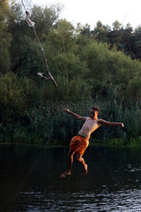 Briescht  Deutschland  Junge laesst sich an einer Badestelle von einem Seil ins Wasser fallen