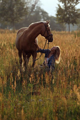 Brieselang  Deutschland  Maedchen hockt auf einer Wiese vor ihrem Pferd und schaut es liebevoll an