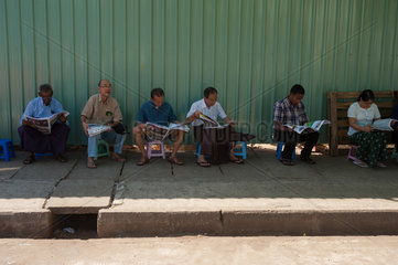 Yangon  Myanmar  Einheimische sitzen am Strassenrand und lesen Zeitung