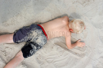 Ein kleiner Junge liegt im Sand