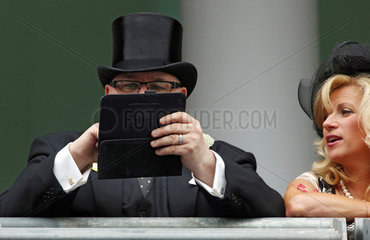 Ascot  Grossbritannien  elegant gekleideter Mann mit Zylinder tippt etwas auf seinem Tablet-PC ein