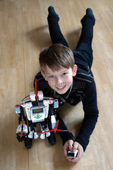 Berlin  Deutschland  Junge liegt stolz neben seinem LEGO-EV3-Roboter auf dem Boden