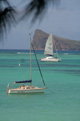 Pereybere  Mauritius  ein fahrender Katamaran und ein ankerndes Segelboot vor der Kueste