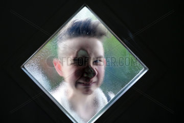 Berlin  Deutschland  Junge schaut durch das Fenster einer Haustuer