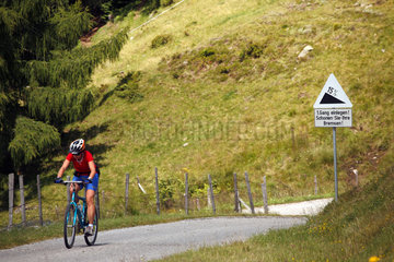 Millstatt  Oesterreich  Frau faehrt mit dem Fahrrad bergauf