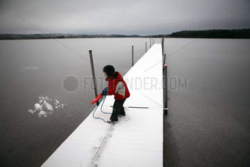 Belloe  Schweden  Kind schippt Schnee von einem Steg in einen See