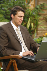 Deutschland  ein junger Mann im Anzug sitzt im Garten an seinem Laptop
