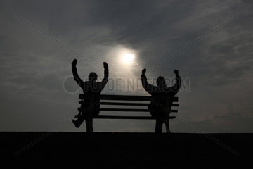 Hannover  Silhouette  Mann und Frau sitzen auf einer Bank und recken die Arme zum Himmel