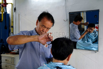 Singapur  Republik Singapur  Strassenfrisoer schneidet einem Kunden die Haare