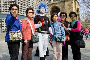 Berlin  Deutschland  koreanische Touristinnen mit einem Strassenkuenstler auf dem Breitscheidplatz