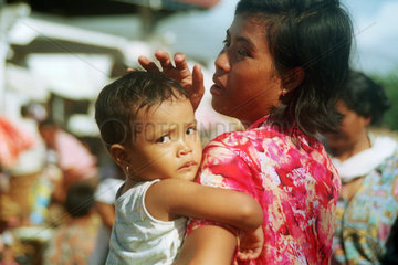 Eine asiatische Frau haelt ihr Kind auf dem Arm
