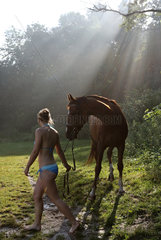 Schwerin  Deutschland  Frau im Bikini und ihr Pferd stehen im Streiflicht auf einer Waldlichtung