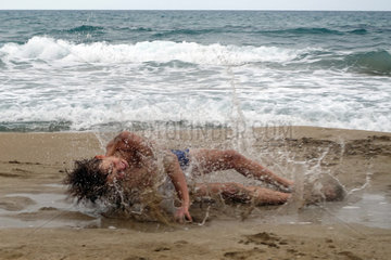 Noto  Italien  Junge laesst sich am Strand von Calamosche in eine Pfuetze fallen