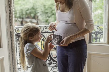 Mother using ultrasound photo to prepare daughter for imminent arrival of new sibling