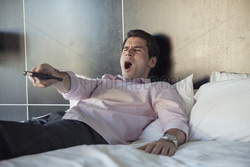 Man lying on bed  yawning while watching TV