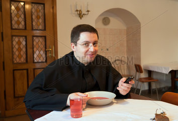 Krakau  Polen  Priester prueft die SMS seines Handys beim Essen