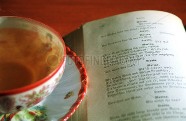 Eine Tasse Tee steht neben einem aufgeklappten Buch.