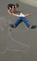 Werl  Deutschland  Junge zeichnet die Umrisse eines Freundes auf eine Strasse