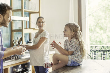 Girl chatting with parents preparing family meal in kitchen