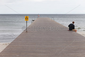 Ystad  Schweden  Mann sitz einsam auf einem Badesteg an der Ostseekueste