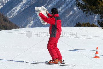 Skilehrer liest Zeitung beim Ski fahren auf der Piste