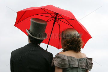 Hannover  Deutschland  elegant gekleidetes Paar steht unter einem roten Regenschirm