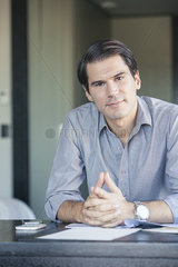 Businessman sitting at desk with clasped hands  portrait