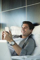 Man relaxing in bed with multimedia smartphone