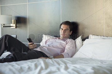 Man unwinding after work by watching TV on bed