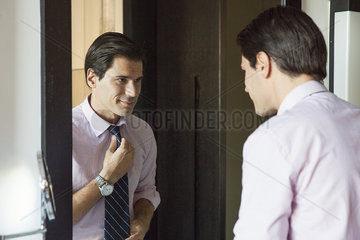 Man looking in mirror  adjusting necktie