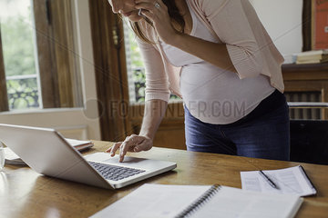 Pregnant woman using laptop computer and making phone call