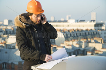 Construction supervisor studying blueprints and talking on cell phone