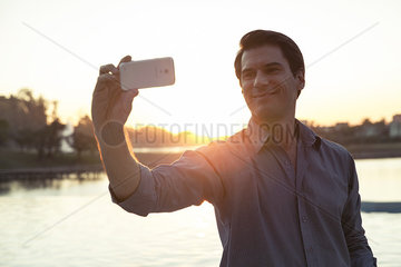 Man using smartphone to photograph himself in front of sunset