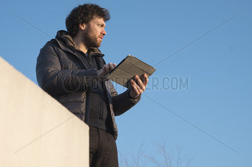 Man holding digital tablet outdoors  looking away in thought