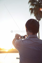 Man photographing sunset with smartphone