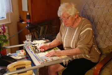 Eine Rentnerin raetselt in einer Raetselzeitung